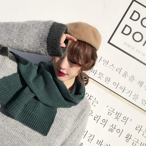 Detail of a dark green knitted scarf worn by a model with a camel beret in chic style