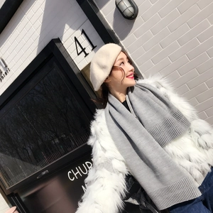 Outdoor shot of a model wearing a thick grey knitted scarf and a beige beret hat