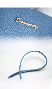 Detail of light blue lychee pattern leather bag with golden Serenity logo and reinforced stitching