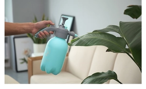 Action shot of blue 2L manual pressure sprayer misting green plant leaves in a home setting