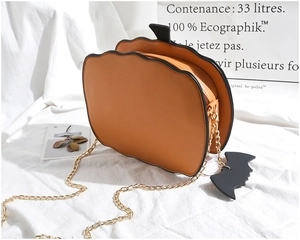 Detailed macro of orange pumpkin bag with gold chain strap and black bat charm