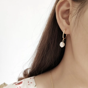 Close-up of a model wearing a gold hoop earring with a baroque freshwater pearl charm