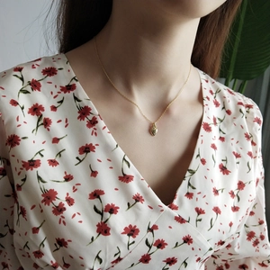 Close-up of a delicate gold heart pendant necklace worn on model with floral top