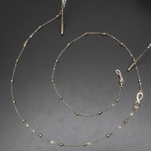 Elegant gold beaded eyewear chain with infinity charm on a black textured background