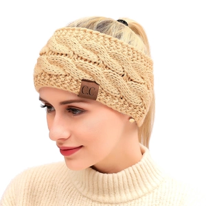Close-up of beige cable knit headband for women with a brown leather logo tag