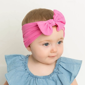 Fascia per capelli neonata in nylon rosa con fiocco su tenera modella dettaglio.