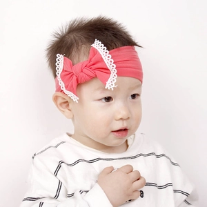 Detail of coral pink baby headband with large bow and white lace trim on an infant model