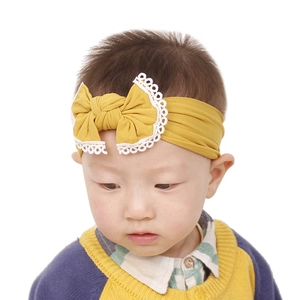 Close-up of yellow baby headband featuring a large bow with white lace trim on an infant