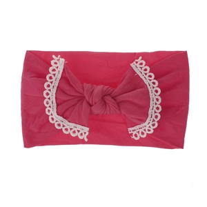Close-up view of a pink soft nylon baby headband with white lace trim and bow detail.