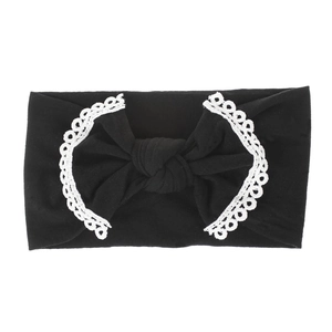 Detail view of a black nylon baby headband with white lace trim and a large soft bow knot