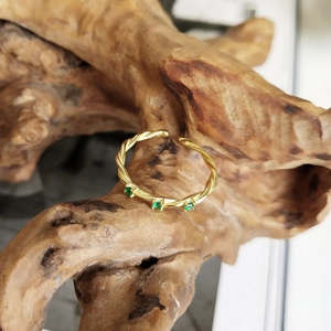 Detail of adjustable gold woven rope ring with three green gemstones on wood