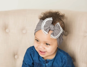 Close-up of a baby girl wearing a soft gray nylon headband with a lace bow detail