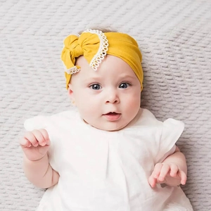 Detail of baby headband in ginger yellow fabric with lace bow on light gray texture