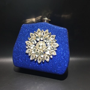 Detail of blue glitter evening clutch with large crystal flower brooch on black background