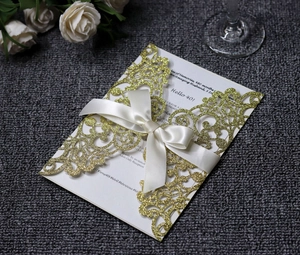 Detail of laser-cut gold glitter invitation with floral pattern and ivory silk ribbon