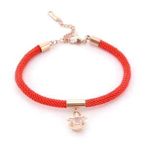 Detail of red braided rope bracelet with rose gold pig charm and inlaid zircon stone