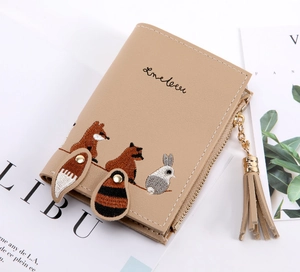 Detail of embroidered forest animals and tassel zipper on khaki faux leather wallet