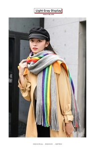 Close-up of thick rainbow striped cashmere-like scarf with fringe on light gray knit