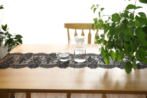 Detail of black eyelash lace table runner on a wooden table with glass carafe and plant