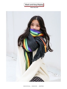 Detail of dark grey knit scarf with vibrant rainbow stripes and long decorative fringes