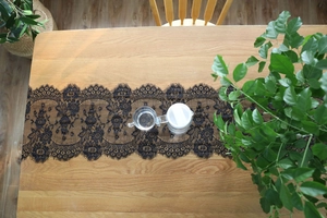 Top view of black eyelash lace table runner on a wooden surface with a glass pitcher