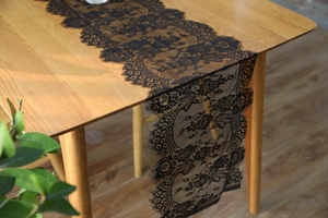 Detail of black eyelash lace table runner with floral patterns on a wooden table