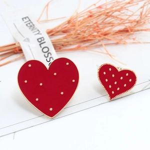 Detail of red enamel heart brooches with gold plating on a minimalist white backdrop