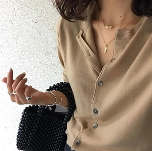 Detail of camel knit cardigan with black buttons and stylish metallic necklace accessory
