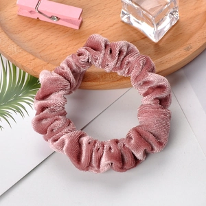 Pink velvet scrunchie with pleated texture on white card with decorative props