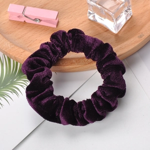 Deep purple velvet scrunchie shown from a top view on a wooden tray with a white background