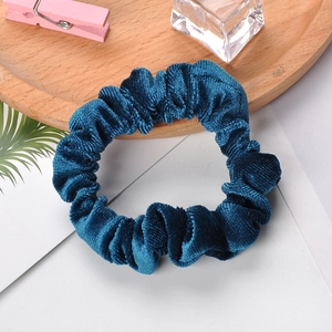 Detailed view of a dark blue velvet scrunchie on a white surface with wooden tray decor