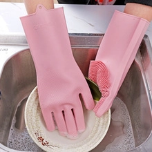 Pink silicone cleaning gloves with scrubbing bristles washing a plate in a kitchen sink