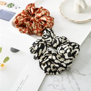 Detailed view of black and orange leopard print satin scrunchies on a marble background