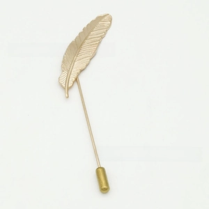 Detail of a golden alloy feather lapel pin with intricate textures and long needle pin