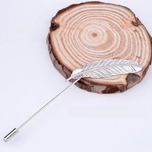 Close-up of silver feather lapel pin with textured metal design on wooden base