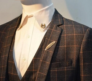 Detailed view of golden feather brooch and horseshoe pin on plaid suit jacket lapel