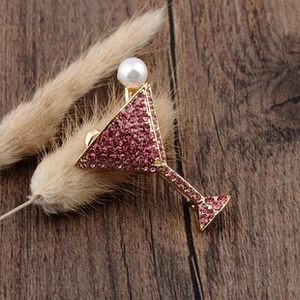 Detailed view of cocktail glass brooch with pink rhinestones and white pearl on gold base