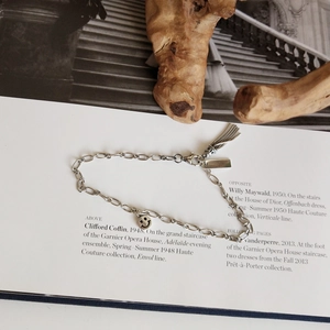 Detail of silver smiley face charm bracelet with metallic tassels on a fashion book background