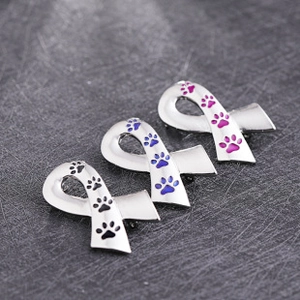 Macro detail of paw print ribbon brooches in pink, blue, and black enamel on silver alloy