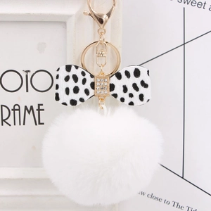 Detailed view of white fluffy pompom keychain with a polka dot bow and gold metal clasp