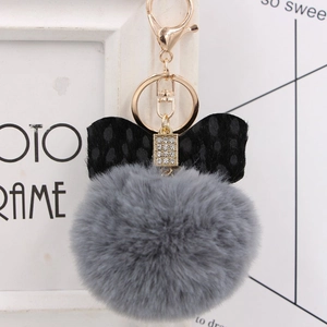 Detail of grey plush pom-pom keychain with leopard bow and gold hardware on a desk