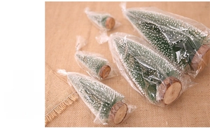Mini frosted Christmas trees with white snow spray and natural wooden bases on burlap cloth