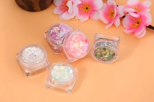 Close-up of five jars of cosmetic glitter gels with star and heart shapes on orange background