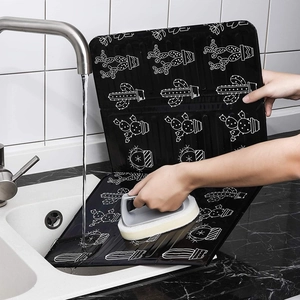 Foldable black aluminum oil splash guard with cactus pattern being washed in a sink