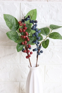 Artificial red and blue blueberry branches in a white ceramic vase for home decor