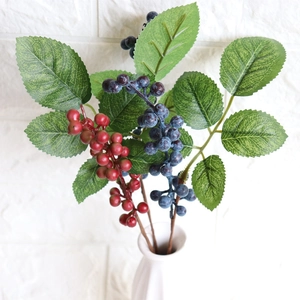Artificial red and blue berry branches with green leaves in a white ceramic vase