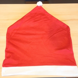 Detailed view of red Santa hat chair cover with white plush pompom on a wooden surface
