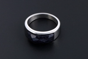 Macro detail of polished stainless steel ring with faceted blue sandstone on black background