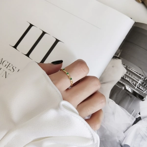 Detailed shot of a twisted gold ring featuring three small green gemstones on a model