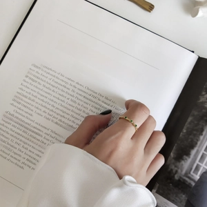 Close-up of elegant gold ring with green gemstone on a model hand with book background